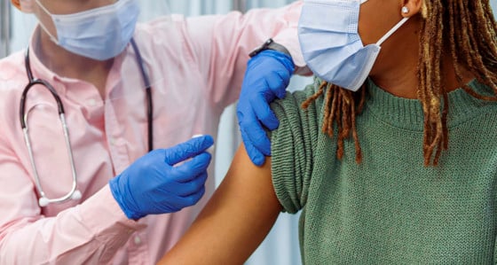A woman with facemask is getting vaccinated by a person wearing PPE