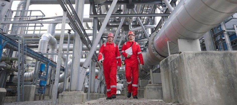 Two men in boiler suits and hard hats walking through a energy facility