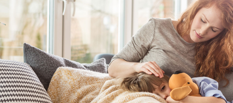 A boy holding a cuddly toy resting on his mother's lap