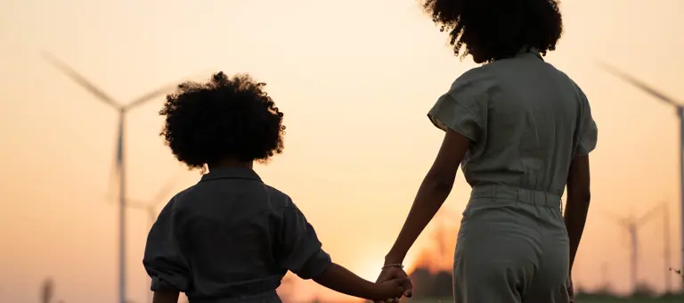 Two people holding hands in front of wind turbines at sunset