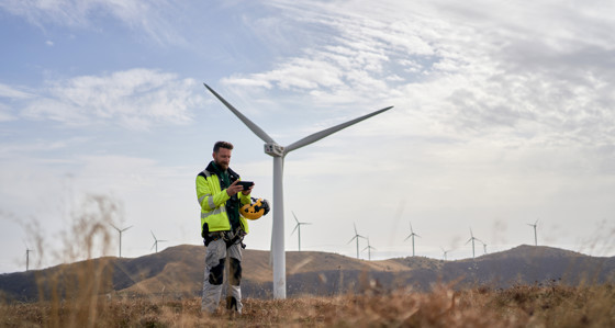 An engineer looking at a tablet in front of wind turbines