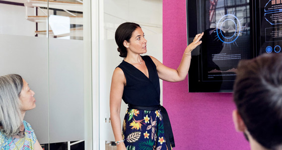 A woman giving a presentation in front of a large touchscreen