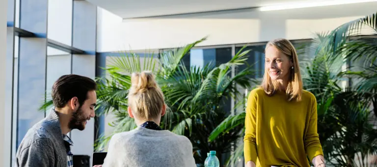 People around a table chatting with a large plant behind them