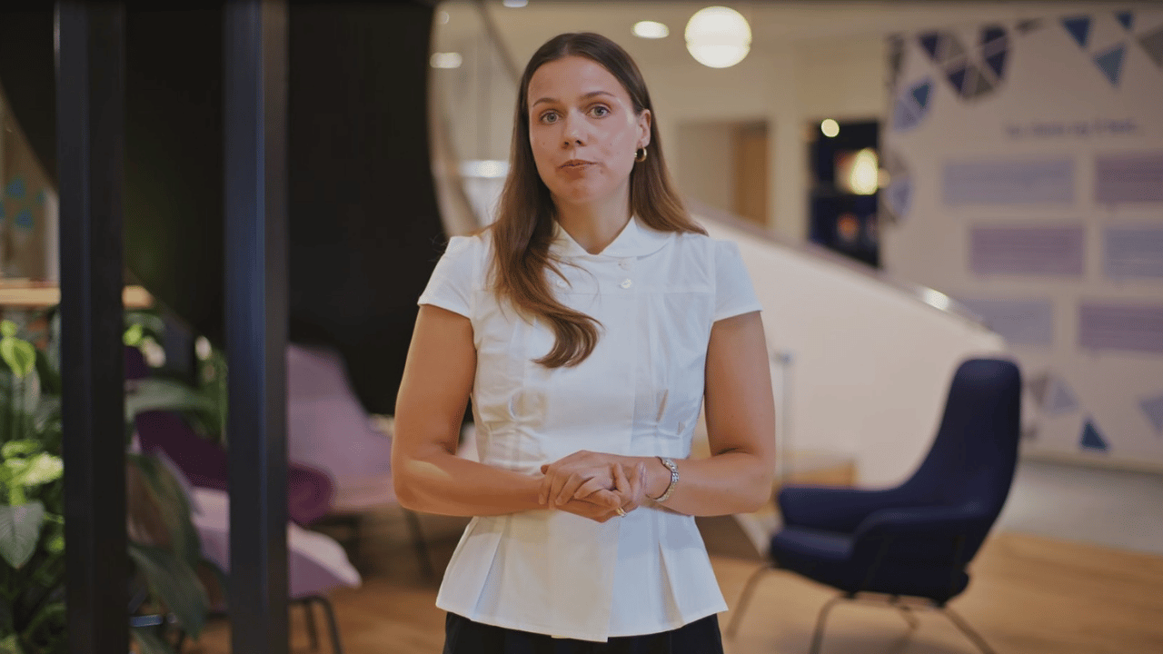 Woman in white shirt standing in a modern office environment facing the camera