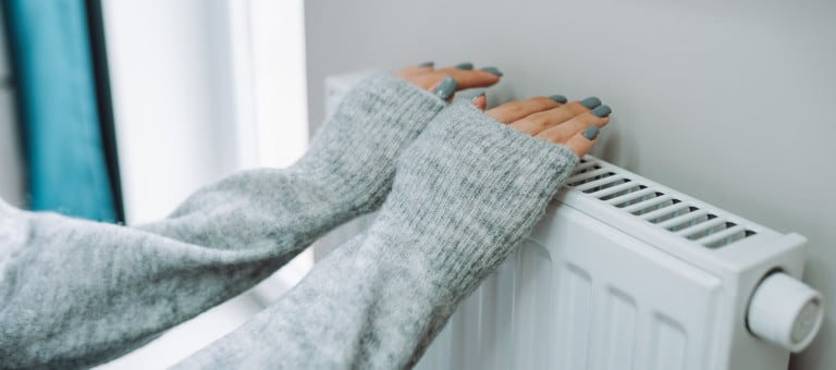A person warming their hands on a radiator