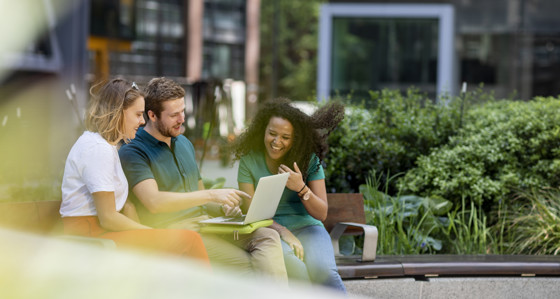 Three people sitting outside looking at a laptop