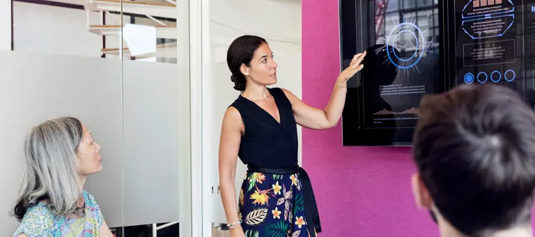 A woman giving a presentation in front of a large touchscreen