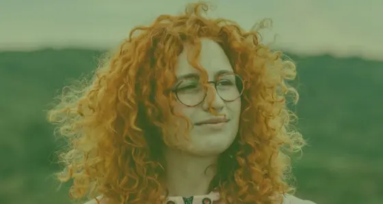 A woman wearing glasses with a hillside in the background