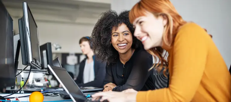 Two interns laughing together while working at their laptops