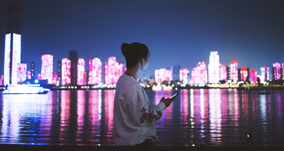 Woman using a mobile phone at night against a city skyline