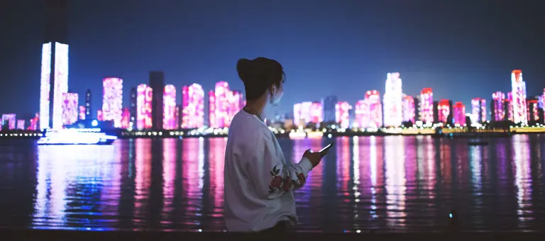 Woman using a mobile phone at night against a city skyline