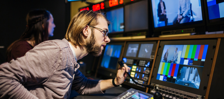 Man operating console in a TV production control room with screens