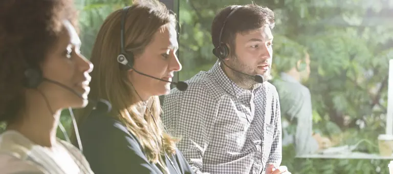 Three colleagues wearing headsets in an office environment