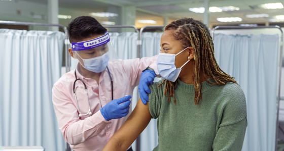 A woman wearing a facemask receiving a vaccine from someone in PPE