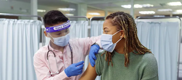 A woman wearing a facemask receiving a vaccine from someone in PPE