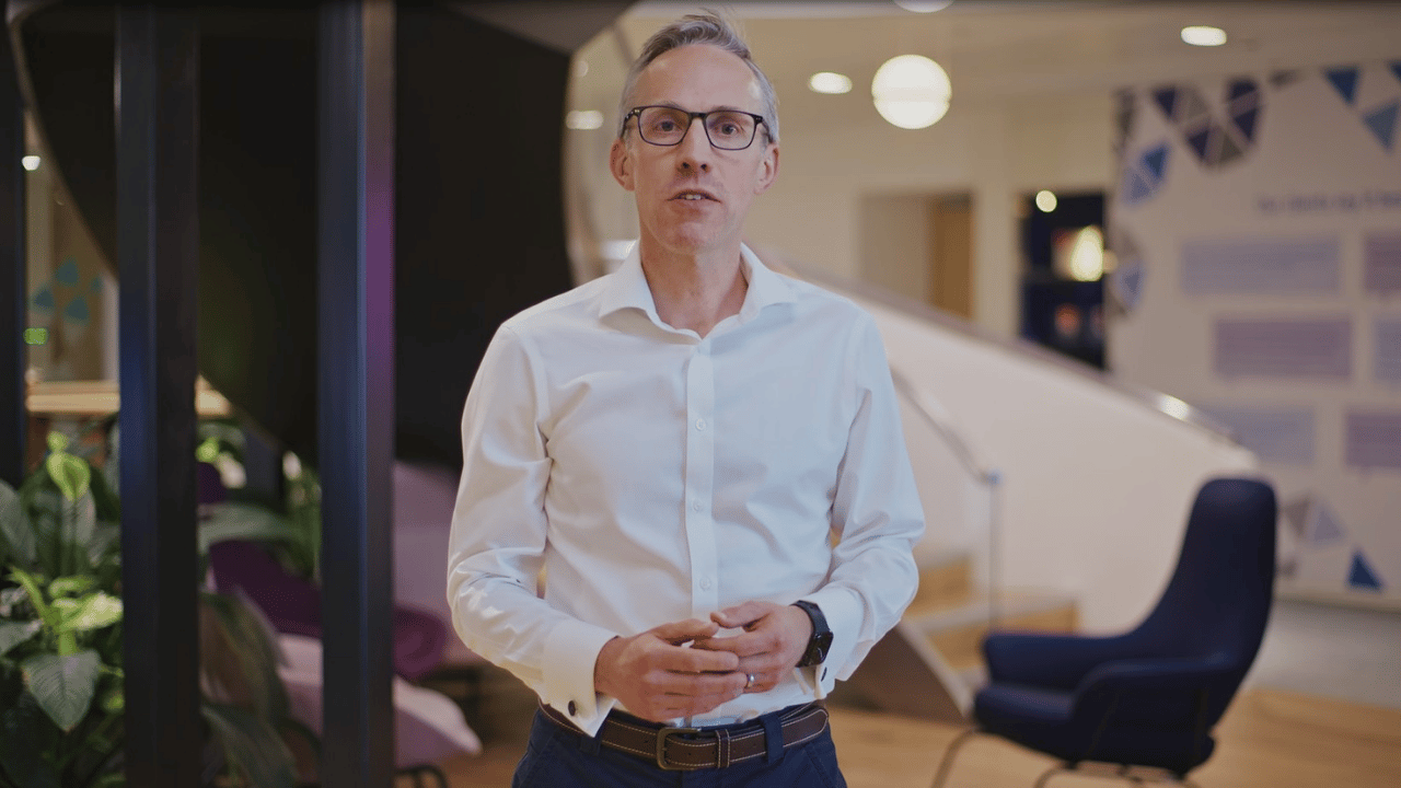Man in white shirt in an office setting speaking directly to the camera