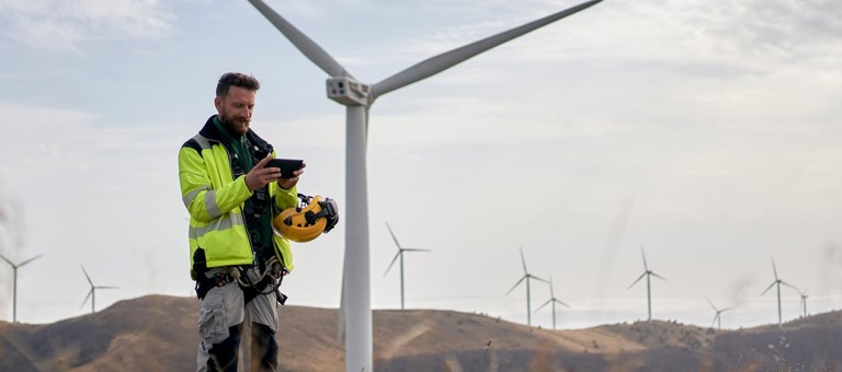 An engineer looking at a tablet standing near to wind turbines