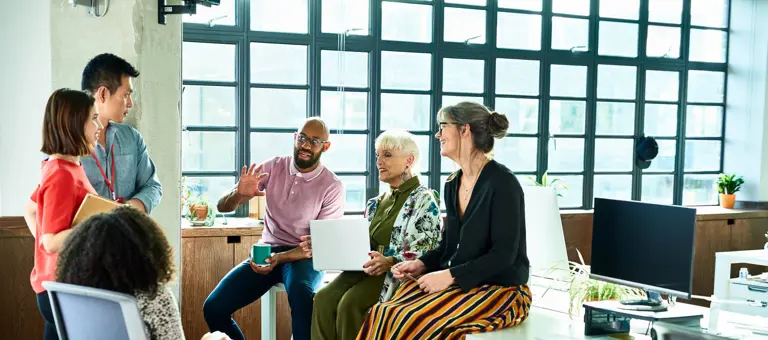 Six people in relaxed conversation with a laptop and coffee