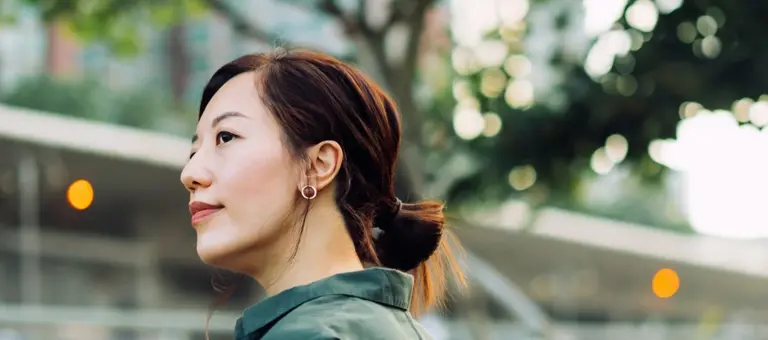 A woman looking thoughtful in front of a tree and building