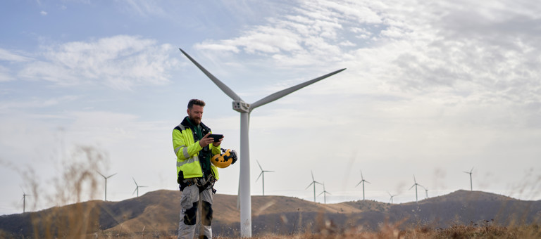 An engineer looking at a tablet in front of wind turbines