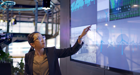 A woman pressing a large touch screen showing wind turbines 