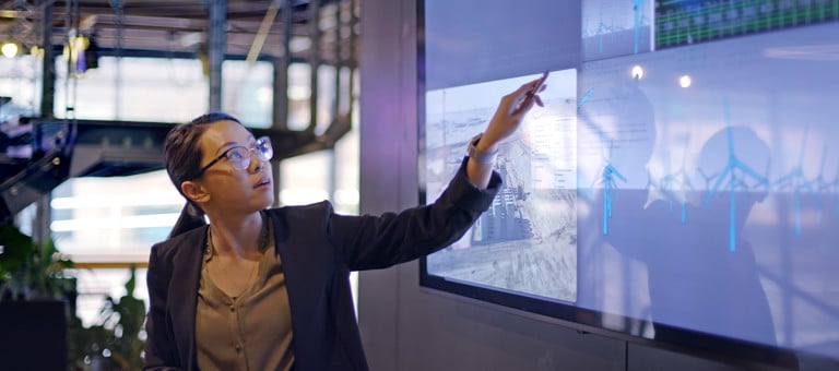 A woman pressing a large touch screen showing wind turbines 
