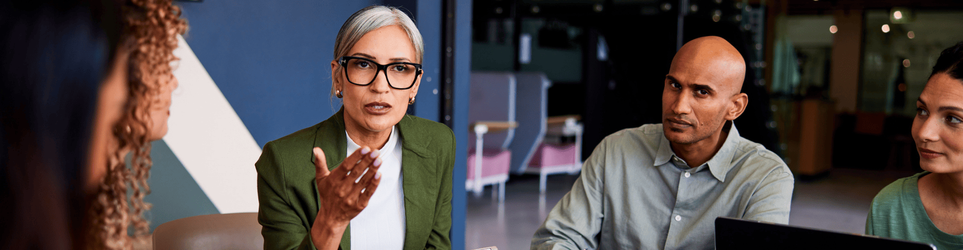 A diverse group of four professionals have a serious discussion around a meeting table.