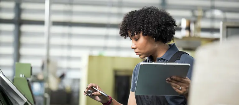 A woman holding a tablet in one hand and a pen and metal ring in the other