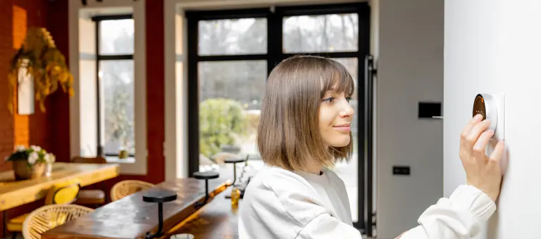 A woman at home adjusting a digital thermostat