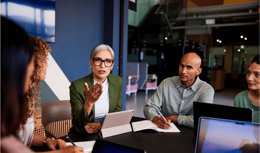 A diverse group of four professionals have a serious discussion around a meeting table.