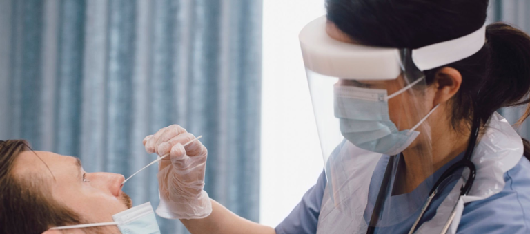 A woman wearing PPE taking nasal swab from a patient