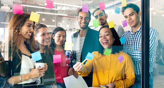 Group of coworkers looking at post-it notes on a glass wall