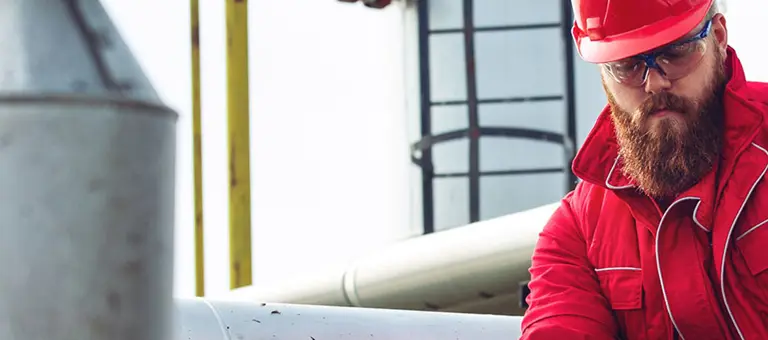 A bearded man in a hard hat working on some large pipes