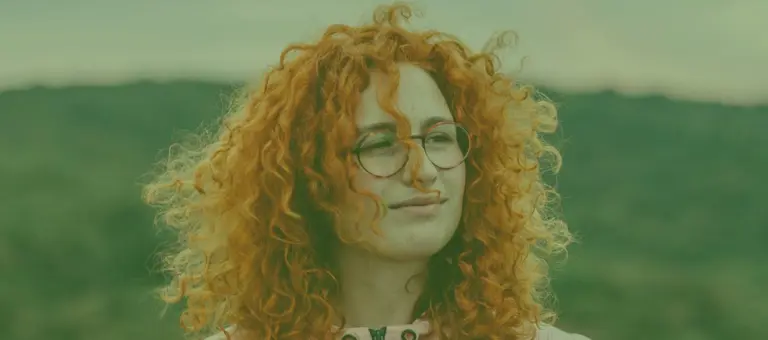 A woman wearing glasses with a hillside in the background