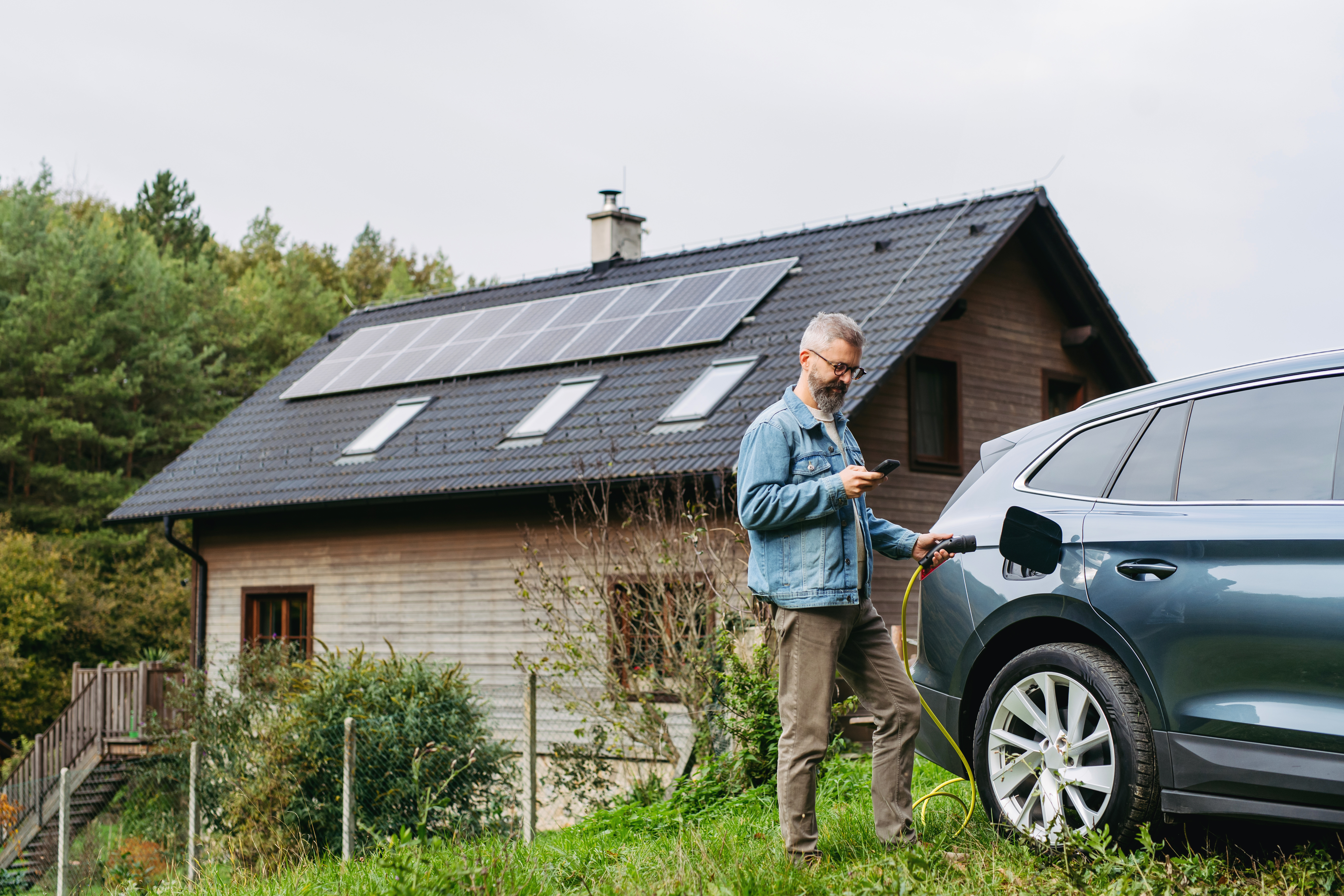 A man charging an electric car at a house with solar panels on the roof