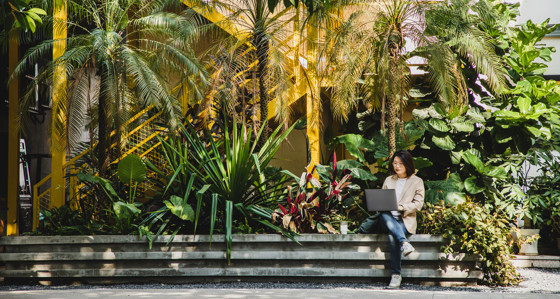 Woman working outside on laptop surrounded by greenery
