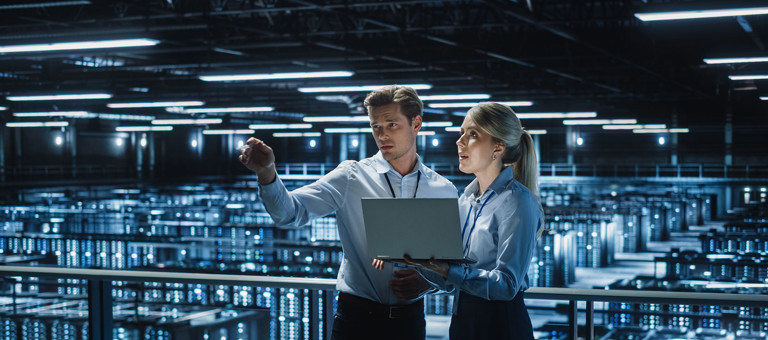 Two colleagues in conversation holding a laptop and standing in a data centre