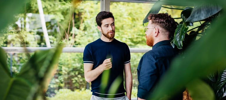 Two men chatting in a greenhouse surrounded by plants