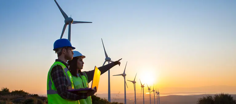 Two engineers with a laptop standing in front of some wind turbines