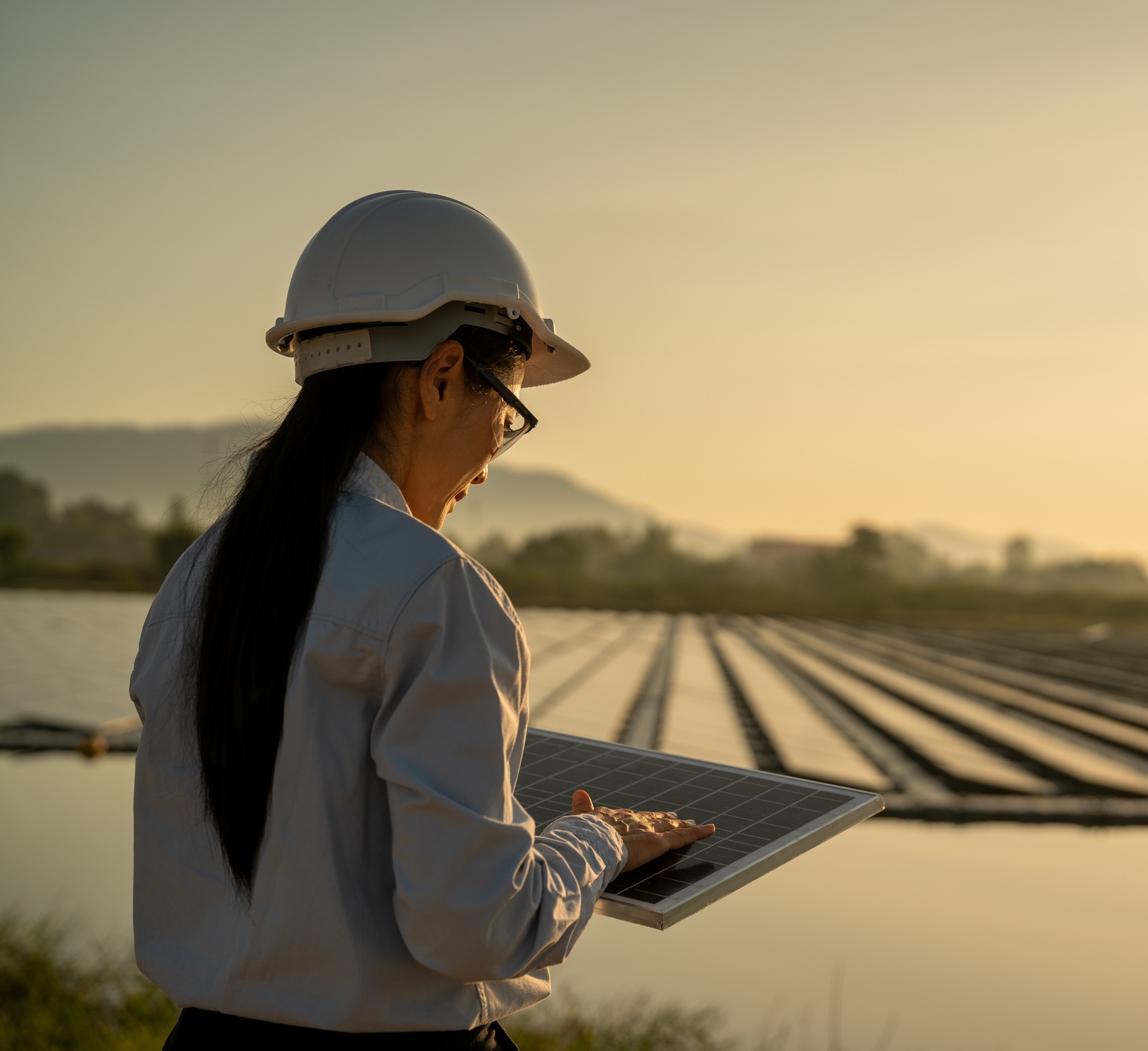 Engineer in a hard hat inspecting a solar panel at a floating solar farm during sunset