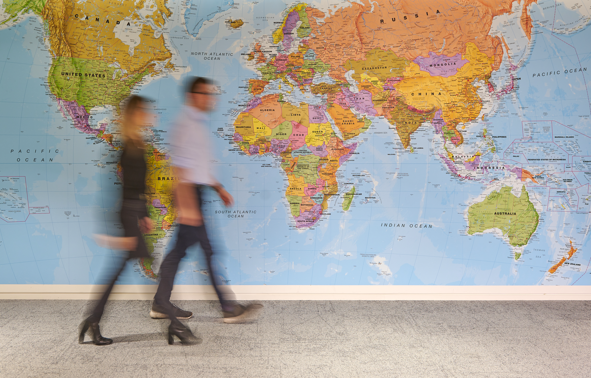 Two people walking in front of a world map