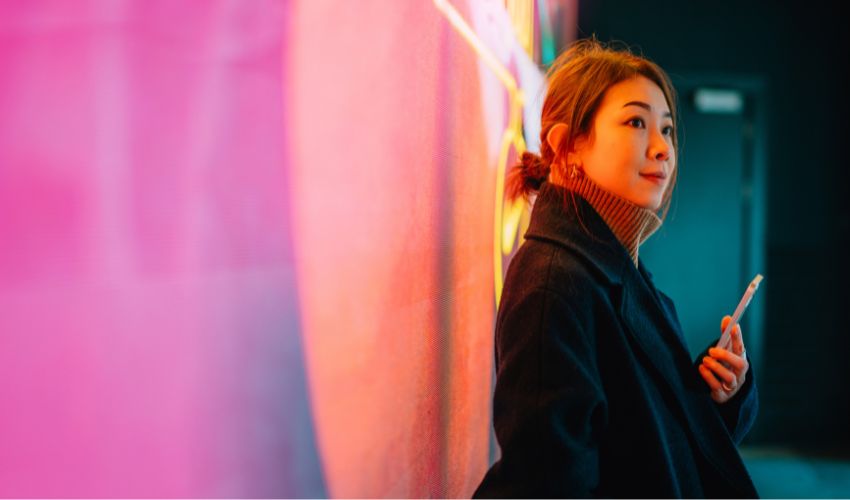 Woman against a pink wall holding a smartphone