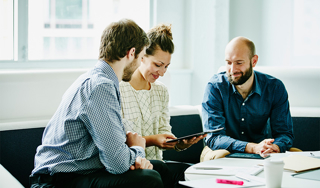 Three smiling colleagues looking at a laptop in a relaxed working environment