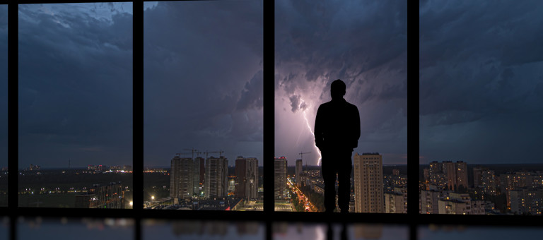 Man in office building looking out at lightning storm