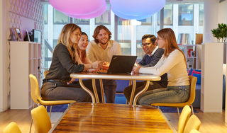 Five colleagues looking at a laptop in a relaxed office environment