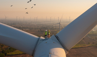 Two men in high-vis jackets and hard hats standing at the top of a wind turbine