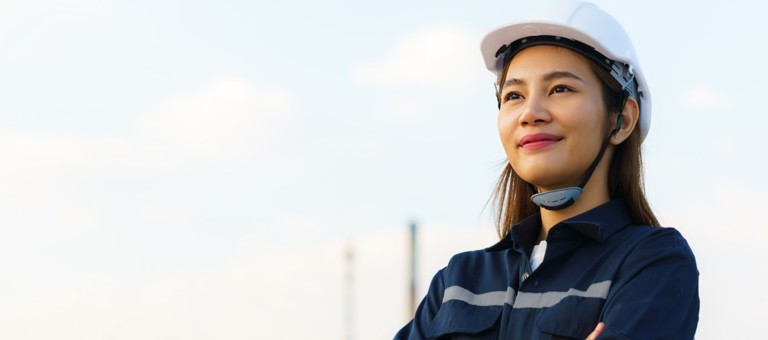 A woman in a hard hat with an industrial landscape in the background