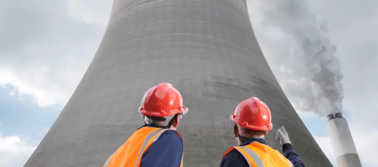 Two men in hard hats staring upwards at a cooling tower
