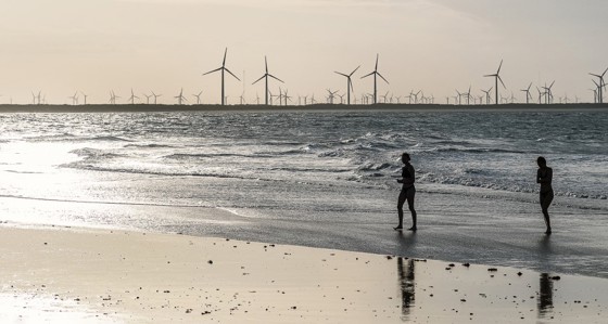 Two people walking on a beach with a windfarm in the distance