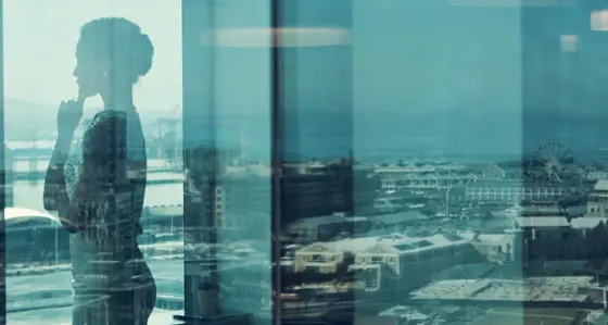 A thoughtful woman looking out of an office window over the city skyline